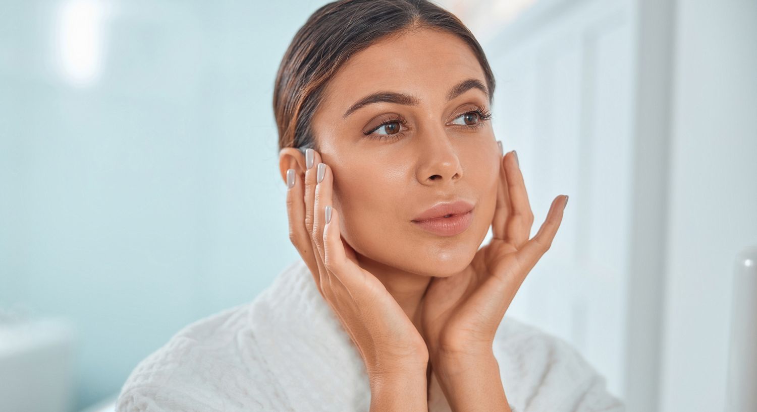 Woman applying skincare in bathroom setting.