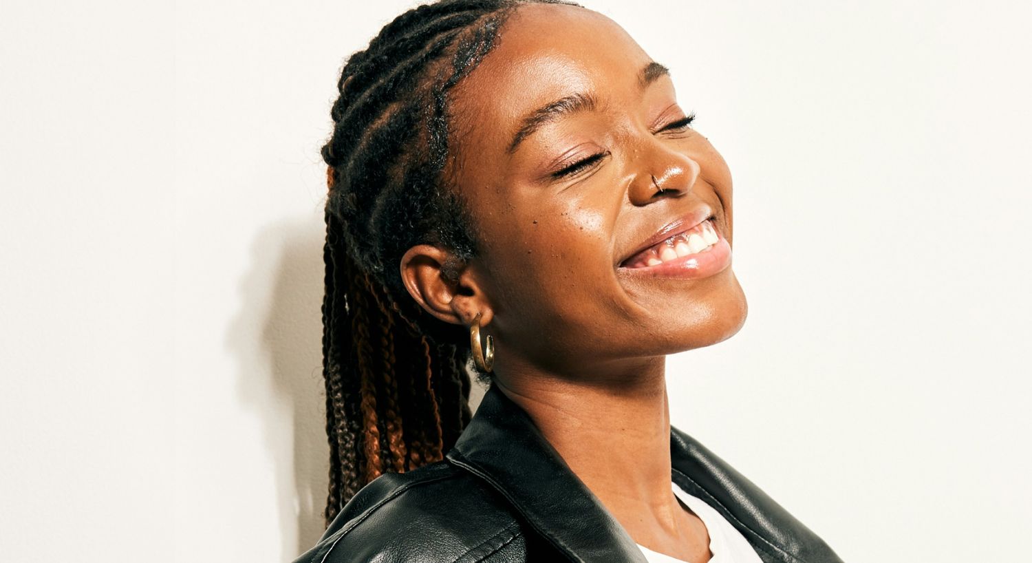 Smiling woman with braided hair in leather jacket.